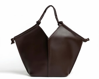 May include: A dark brown tote bag with a distinctive geometric shape. The bag has a single handle and is made from angular panels. Knotted details are present at the handle's base and on the sides, adding a stylish element to the bag's design.