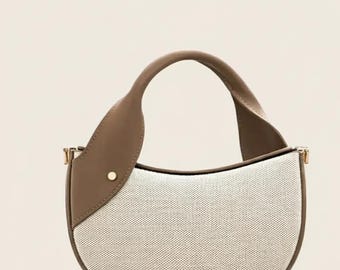 May include: A half-moon handbag with a canvas body and a brown leather handle. The bag features a curved design with a brown leather accent on the side and gold-coloured hardware.
