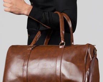 May include: A brown leather duffel bag with two top handles and a side zipped pocket. The bag has a glossy finish and a rectangular shape, suitable for travel or gym use.