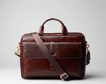 May include: A brown leather briefcase with a top handle and a detachable shoulder strap. The bag has a front pocket and gold-coloured hardware. The leather has a polished finish, and the bag appears to be new.