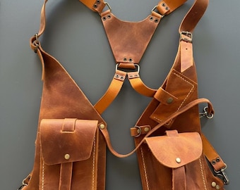 May include: A brown leather chest harness with two front pockets and adjustable straps. The harness features metal hardware and a symmetrical design. The leather has a distressed appearance, suggesting a vintage or rustic style.
