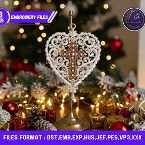 May include: An embroidered heart design with a cross, displayed on a gold stand. The design is white and brown. The text "3 SIZE EMBROIDERY FILES" is visible. The background includes Christmas decorations and fairy lights, creating a festive scene.