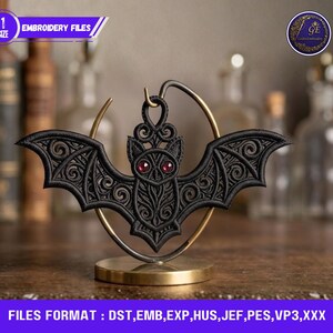 May include: Black embroidered bat with red gem eyes, displayed on a gold-colored stand. The bat has intricate wing and body details. The image includes the text "EMBROIDERY FILES" and "FILES FORMAT: DST, EMB, EXP, HUS, JEF, PES, VP3,XXX".