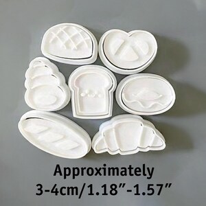 May include: A set of white plastic cookie cutters in various bread shapes, including a pretzel, croissant, and loaf of bread. The text "Approximately 3-4cm/1.18"-1.57"" is displayed below the cutters.
