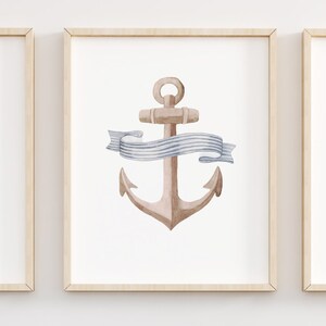 May include: Three watercolor paintings in wooden frames. The first painting features a blue and white striped lighthouse. The second painting features a brown anchor with a blue and white ribbon. The third painting features a blue sailboat with a white sail.