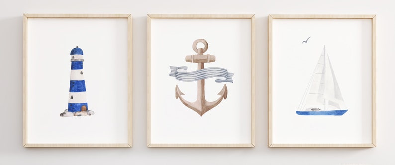 May include: Three watercolor paintings in wooden frames. The first painting features a blue and white striped lighthouse. The second painting features a brown anchor with a blue and white ribbon. The third painting features a blue sailboat with a white sail.
