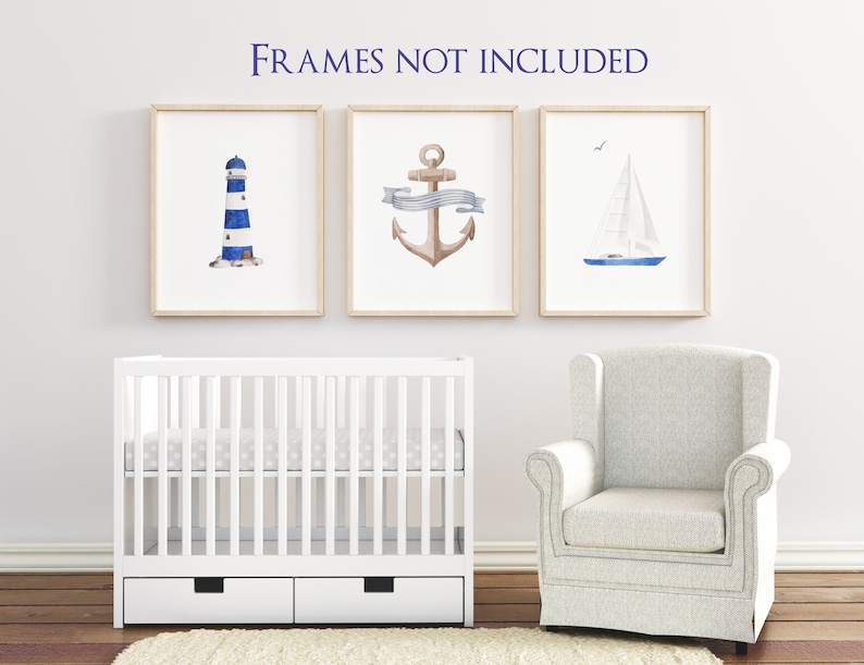 May include: Three watercolor prints in white frames depicting nautical themes: a lighthouse, an anchor, and a sailboat. The prints are displayed on a white wall above a white crib and a white armchair.