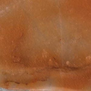 May include: Close-up of a section of a stone with a warm, earthy color palette. The surface displays a blend of orange, tan, and brown hues, with subtle variations in tone and texture. The stone's natural patterns create a visually interesting and organic appearance.