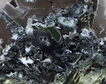 May include: Abstract image of a stone surface with a complex pattern. The stone features a mix of dark green, black, white, and brown colors, creating a marbled effect. The design includes swirling patterns and areas of solid color.