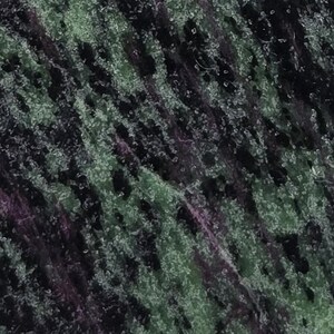 Pode incluir: Close-up de uma superfície de pedra com um padrão manchado. A pedra apresenta uma mistura de tons verde escuro, preto e roxo, criando uma aparência texturizada. O efeito geral é uma estética natural e orgânica.