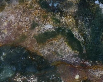 May include: Close-up of a natural stone surface with a blend of colors. The stone features a mix of dark green, brown, and white hues, creating a textured and organic appearance. The pattern resembles a landscape with flowing lines and varied tones.