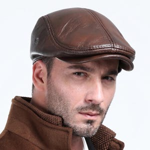 Puede incluir: Gorra de estilo newsboy de cuero marrón, con una corona redondeada y una visera corta y rígida. La gorra tiene un acabado liso y brillante y un diseño clásico. Un accesorio de moda elegante.