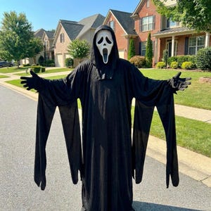May include: A full-length black hooded robe with long, wide sleeves and matching black gloves. The costume includes a white plastic mask featuring a stylised elongated face with black eye sockets and an open, oval-shaped mouth, mimicking a ghost.