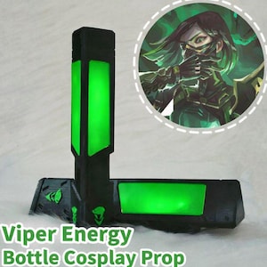 May include: Black and green Viper Energy Bottle Cosplay Prop. The prop has a rectangular shape with a green glowing section. The text "Viper Energy Bottle Cosplay Prop" is printed on the bottom. A circular image of a character is in the background.