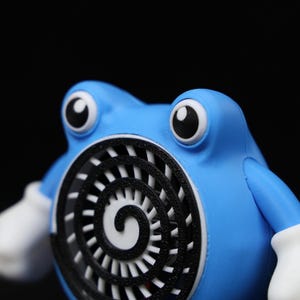 Pode incluir: Figura azul de um personagem de desenho animado com olhos grandes e redondos e luvas brancas. O personagem tem um design de espiral branco e preto no peito. A figura est&aacute; em um fundo preto.