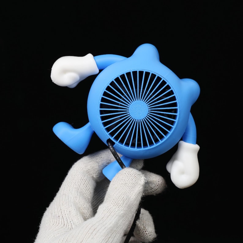 Pode incluir: Um ventilador port&aacute;til azul caprichoso em forma de personagem de desenho animado, com um design de ventilador circular e l&acirc;minas pretas. O ventilador tem m&atilde;os e p&eacute;s com luvas brancas. Um cabo de alimenta&ccedil;&atilde;o preto est&aacute; conectado.