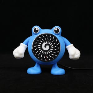 Pode incluir: Um ventilador azul, semelhante a um desenho animado, com luvas e p&eacute;s brancos. O ventilador tem um design em espiral no centro e olhos grandes e redondos. O ventilador est&aacute; ligado a um cabo preto.