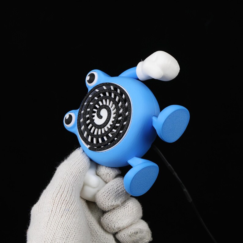 Pode incluir: Uma figura azul, semelhante a um desenho animado, com um design em espiral na frente. Tem dois olhos, dois p&eacute;s e uma luva branca. A figura &eacute; segurada contra um fundo preto.