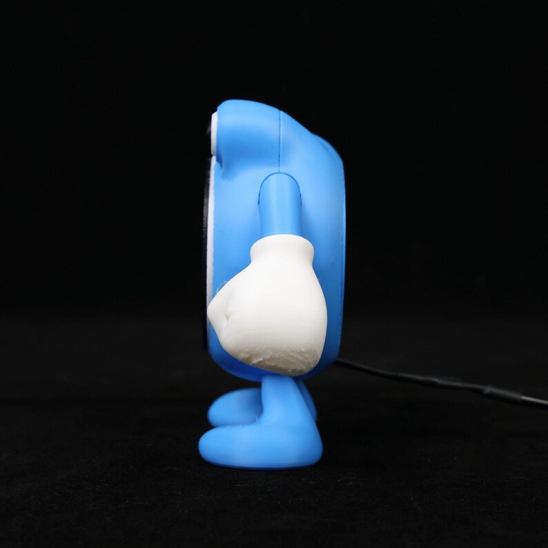 Pode incluir: Uma figura azul semelhante a um desenho animado com luvas e p&eacute;s brancos. A figura tem um corpo arredondado e um pequeno rosto circular. Um cabo preto estende-se da parte inferior da figura.