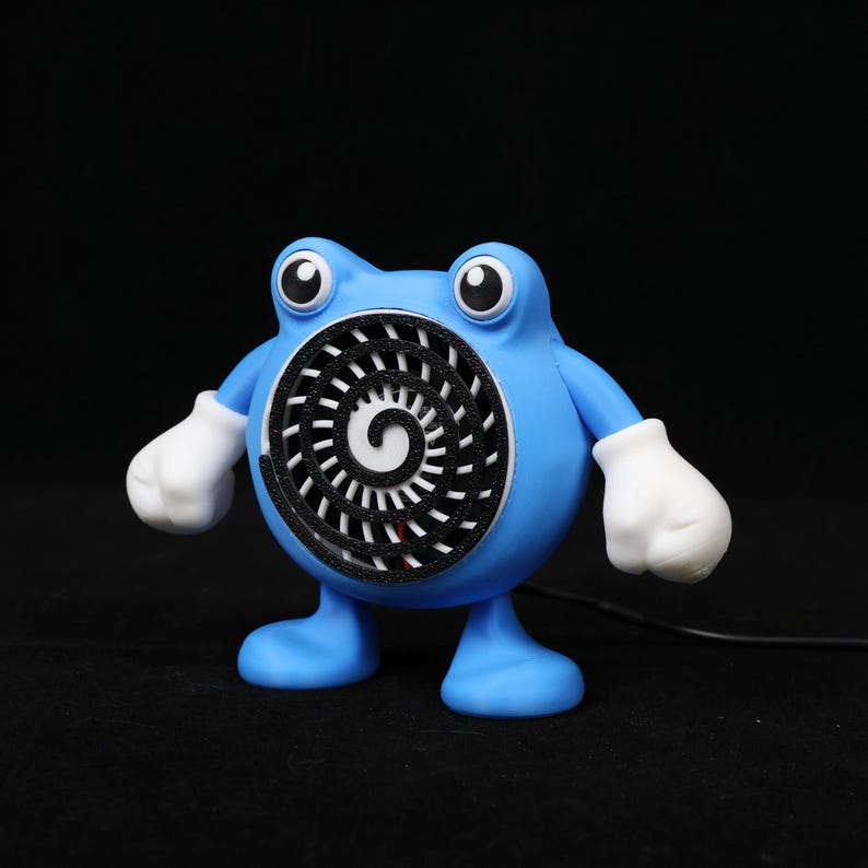 Pode incluir: Uma figura azul, semelhante a um desenho animado, com um design em espiral na frente. A figura tem luvas brancas e olhos grandes. O fundo &eacute; preto.