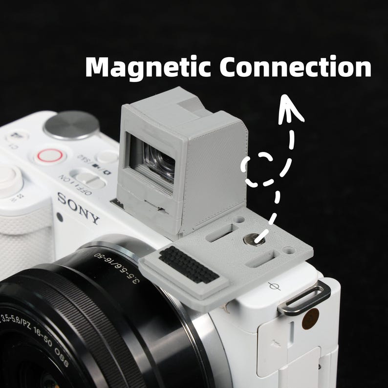 May include: A gray camera viewfinder attached to a white Sony camera. The viewfinder is connected via a magnetic plate. The text "Magnetic Connection" is displayed above the viewfinder.