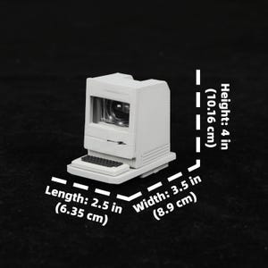 May include: A miniature, off-white computer model with a screen and keyboard. The model is 4 inches (10.16 cm) tall, 2.5 inches (6.35 cm) long, and 3.5 inches (8.9 cm) wide. The computer has a retro design.