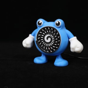 Pode incluir: Uma figura azul, semelhante a um desenho animado, com um design em espiral no peito. A figura tem luvas e p&eacute;s brancos, e olhos grandes e redondos. O fundo &eacute; preto, destacando as cores vibrantes da personagem.