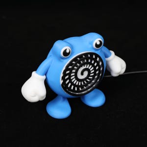 Pode incluir: Uma figura azul com luvas e olhos brancos. A figura tem um desenho em espiral preto e branco na barriga. A figura est&aacute; em p&eacute; sobre dois p&eacute;s azuis e tem dois bra&ccedil;os. O fundo &eacute; preto.