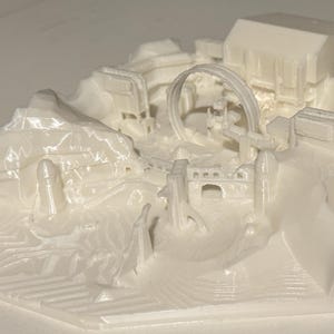 Könnte beinhalten: Ein 3D-gedrucktes Architekturmodell in Off-White. Das Modell zeigt eine Landschaft mit Gebäuden, Bögen und einer Achterbahn-ähnlichen Struktur. Das Design umfasst geschichtetes Gelände und verschiedene architektonische Elemente.