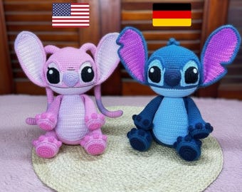 May include: Two crocheted plush toys, one pink and one blue, resembling cartoon characters. The pink toy has large ears and a long tail. The blue toy has large ears and a round body. Both toys have large black eyes and are sitting on a woven mat.
