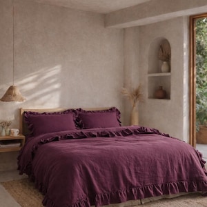 以下が含まれることがあります： 深い紫色の掛け布団カバーと、お揃いの枕カバーがセットされたベッド。 寝具にはフリルの縁取りがあります。 ベッドは、ニュートラルな色調の寝室にある天然繊維のラグの上にあります。