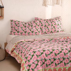 May include: A bed set featuring a floral pattern in pink and green on a white background. The set includes a quilt and two pillowcases. The quilt has a border with a similar floral design. The bedding is made of a soft, comfortable material.