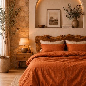 May include: A bedroom with warm tones features an orange duvet cover and pillows on a wooden bed frame. A wooden nightstand with a lamp sits beside the bed. A framed picture and vase with greenery are on a shelf above the bed.