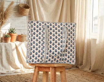 May include: A large tote bag with a cream background and a repeating blue floral pattern. The bag has two cream-colored handles and is sitting on a wooden stool. The bag is made of a quilted material.