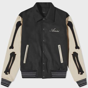 May include: Black varsity jacket with bone-shaped appliqués on the cream-colored sleeves. The jacket features a button-up front, a collar, and the word "Amiri" embroidered on the chest. The cuffs and hem have a striped design.
