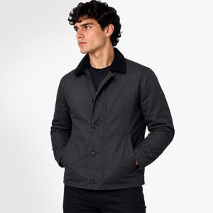 May include: A charcoal grey jacket featuring a black collar, a front button closure with four visible buttons, and two side pockets. The jacket is constructed with long sleeves and a straight hemline, providing a structured and clean appearance.