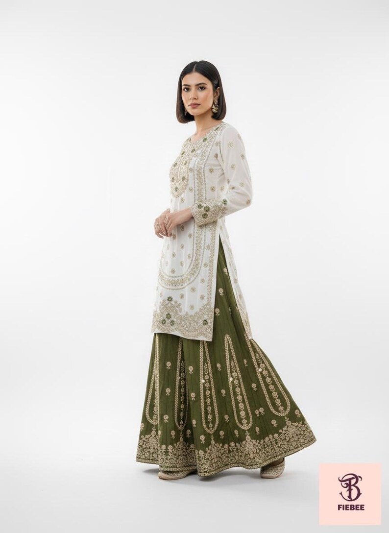 May include: A white tunic and olive green skirt ensemble with intricate gold embroidery. The long-sleeved tunic features detailed patterns around the neckline, sleeves, and front. The skirt has a flowing silhouette with matching embroidery. The outfit is a traditional style.