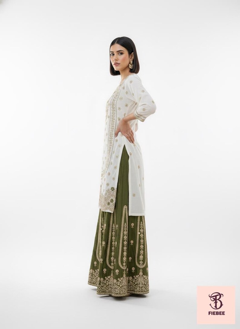 May include: A white tunic with gold embroidery and three-quarter sleeves is paired with a long olive green skirt. The outfit features detailed gold patterns and is suitable for special occasions.