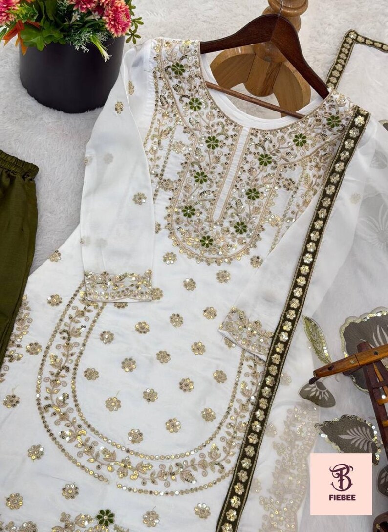 May include: White embroidered tunic and matching scarf with gold and green floral designs. The long-sleeved top features intricate embroidery around the neckline and cuffs, with a matching scarf. Olive green trousers are visible on the left.
