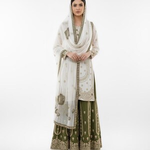 May include: A sophisticated outfit comprising a white tunic and head covering, embellished with detailed gold embroidery. The ensemble is complemented by a long, olive green skirt, offering a culturally rich aesthetic. The outfit is from Fiebee.