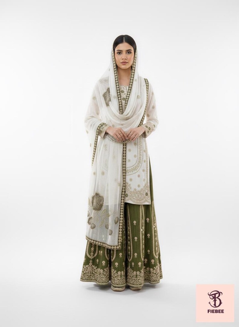 May include: A sophisticated outfit comprising a white tunic and head covering, embellished with detailed gold embroidery. The ensemble is complemented by a long, olive green skirt, offering a culturally rich aesthetic. The outfit is from Fiebee.