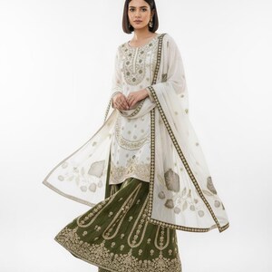 May include: An embroidered white and olive green salwar kameez outfit. The ensemble features a long-sleeved tunic, wide-legged trousers, and a matching dupatta. The gold embroidery decorates the neckline, sleeves, and hem, creating a formal appearance.