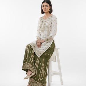 May include: A white embroidered tunic and olive green palazzo trousers. The tunic has long sleeves and gold embroidery. The trousers have a wide leg and matching gold embroidery. The outfit is worn with gold flats.