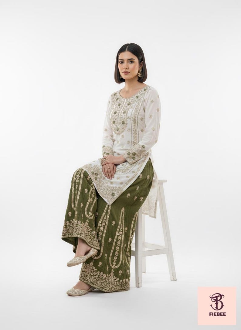 May include: A white embroidered tunic and olive green palazzo trousers. The tunic has long sleeves and gold embroidery. The trousers have a wide leg and matching gold embroidery. The outfit is worn with gold flats.