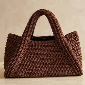 Peut inclure: Un sac à main marron foncé réalisé avec un motif de points au crochet dense et texturé. Le sac présente une base rectangulaire structurée, deux anses intégrées sur le dessus et un tissage uniforme sur toute la surface extérieure.