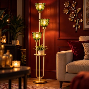 May include: A tall floor lamp with a gold-toned metal frame featuring three tiered, green glass, flower-shaped shades. A small white potted plant sits on a circular shelf integrated into the center of the lamp structure, which stands on a round base.