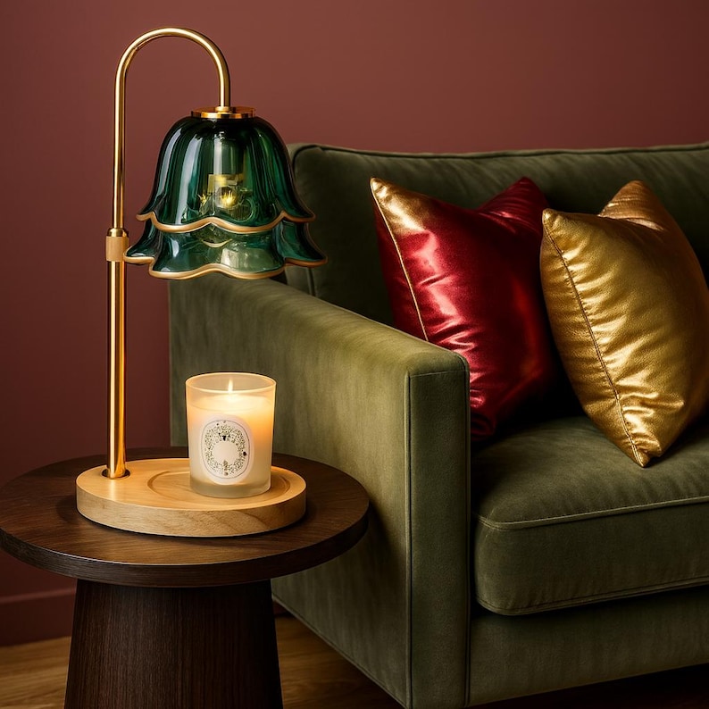 May include: A decorative table lamp with a green glass shade and gold-colored metal accents. A lit candle sits on a wooden tray below the lamp. The lamp is next to a green sofa with red and gold pillows.