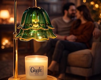 May include: A candle warmer with a green glass shade and a gold-colored metal frame. The shade is shaped like a flower. A lit candle in a glass jar sits on a wooden base. The candle jar has the word "Giggle" on it.