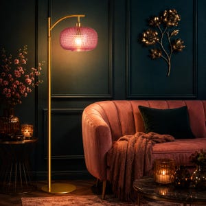 May include: A floor lamp with a slender gold metal stand and a round base, featuring a textured, translucent pink glass shade. The lamp emits a warm glow, illuminating the surrounding space with a soft, diffused light from its central bulb.
