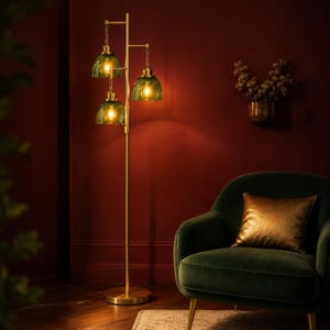 May include: A floor lamp with a tall, slender brass-colored metal stand and a circular base. The lamp features three hanging light fixtures with translucent, wavy-edged green glass shades that emit a warm, glowing light from within.